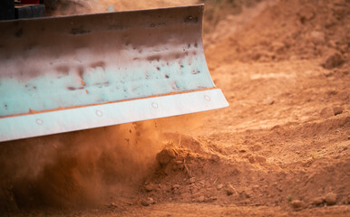 Construction tractor with specialized dozer blade pushing and grading soil at excavation site. Heavy machinery transforming raw land into prepared foundation for upcoming building development project.