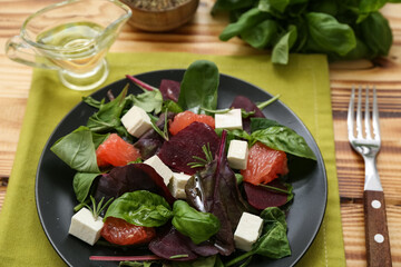 Plate with healthy vegetable salad, napkin, fork and gravy boat of oil on wooden background