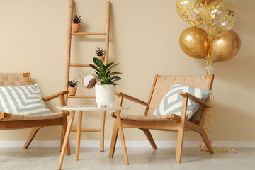 Beautiful golden air balloons with chairs and coffee table near beige wall at home