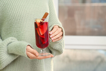Young woman holding glass cup of hot mulled wine at home, closeup