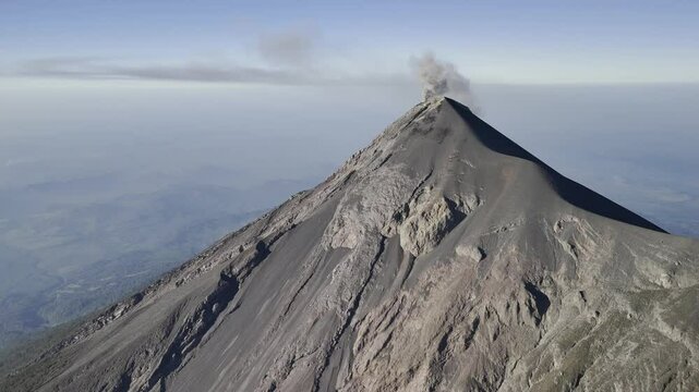 Drone approaches the top of El Fuego Volcano as it smokes in the morning light in Guatemala