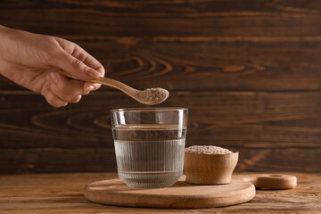 Female hand adding psyllium husk into glass of water on wooden background