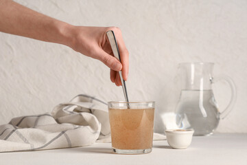 Female hand with spoon and psyllium husk in glass of water on light background
