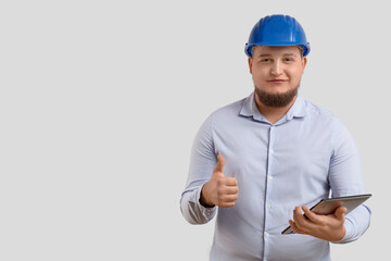 Male engineer with tablet computer showing thumb-up gesture on light background
