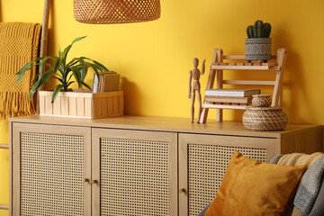 Interior of living room with chest of drawers near yellow wall