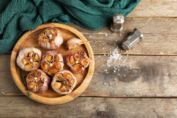 Tray with baked garlic, rosemary and thyme on wooden background