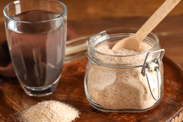 Jar with psyllium husk powder and glass of water on table, closeup