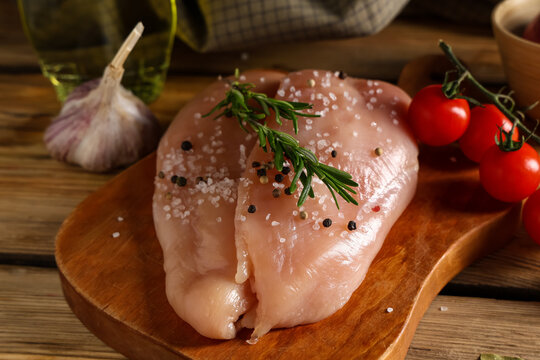 Board of raw chicken breast with different spices and fresh tomatoes on wooden background