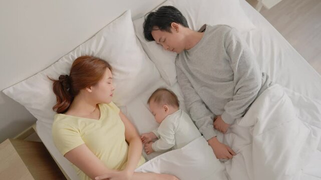 Asian young parents sleep with baby boy on bed in cozy bedroom at home.