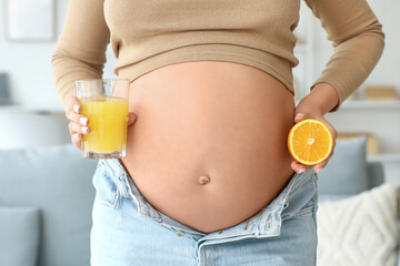 Young pregnant woman with glass of juice and orange at home, closeup