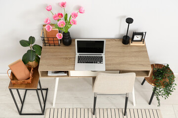 Interior of modern workplace with stools, houseplants, laptop and beautiful tulip flowers in vase,...