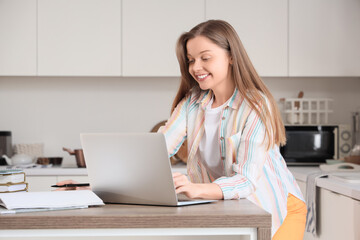 Teenage girl with laptop working online at table in kitchen