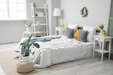 Interior of festive bedroom with big bed, bedside tables, shelving unit and Easter decorations