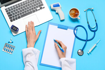Female doctor's hands with stethoscope, laptop and cup of coffee writing in clipboard on blue background. World Health Day