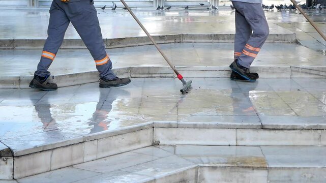 Workers clean large public plaza with mops in early morning light