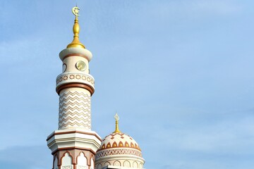 A beautiful mosque with an elegant minaret and dome under a clear blue sky. The intricate Islamic architecture and golden crescent create a serene spiritual atmosphere, symbolizing faith and devotion.