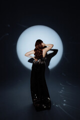 A woman in a metallic dress poses under a dramatic spotlight. Her confident stance and artistic...