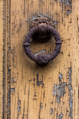 Detail of a wooden door with pealing yellow paint with  rusty door knocker