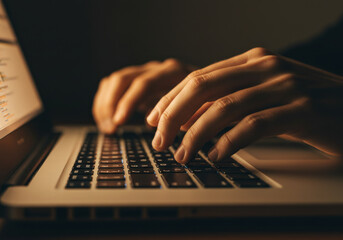 A person typing on a laptop at a desk in a bright room, focused and determined.