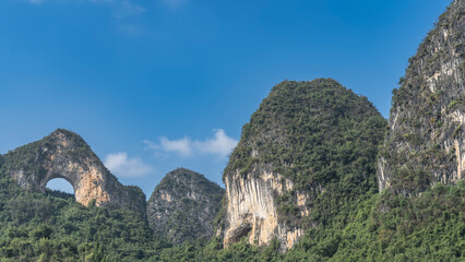 Picturesque karst mountains against a clear blue sky. Round arched hole at the top. Green...