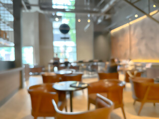 Blurred interior of a modern cafe with wooden chairs and tables, warm lighting, and large windows, creating a cozy and inviting atmosphere for social gatherings and relaxation.