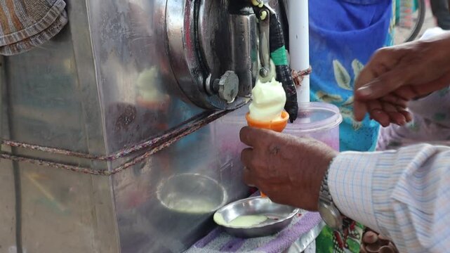 An Indian street vendor crafts softy ice cream in a crunchy cone, topped with colorful fruit cubes, blending creamy sweetness with fresh, vibrant flavors