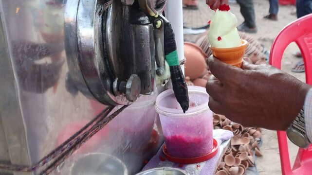 An Indian street vendor crafts softy ice cream in a crunchy cone, topped with colorful fruit cubes, blending creamy sweetness with fresh, vibrant flavors