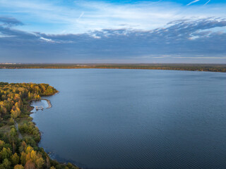 Fototapeta premium Autumn forest on lake shore at sunset and city on horizon, auerial view