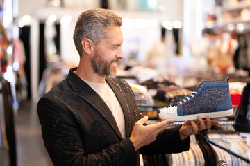 Footwear for man. Fashion sneakers. Stylish man in footwear boutique. Mature man choosing footwear sneakers shoes. Designer footwear with rhinestones selection. Luxury male style and glamour.