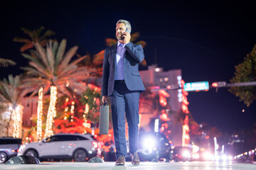 Business man with briefcase and phone walking at city. Rich man in suit in night. Business man on street. Business man walking near night city. Business style. Rich businessman in luxury setting.