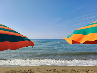 Orange and green beach umbrellas. Blue sky. Relaxing context. Summer holidays at the sea. General contest and location