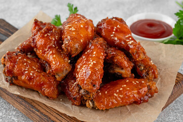 Baked chicken wings in a sweet chili sauce and sesame seeds on a wooden board on a concrete background. Close up.