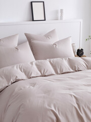Double bed with fluffy duvet in a beige duvet cover and four pillows close-up side view vertical photo