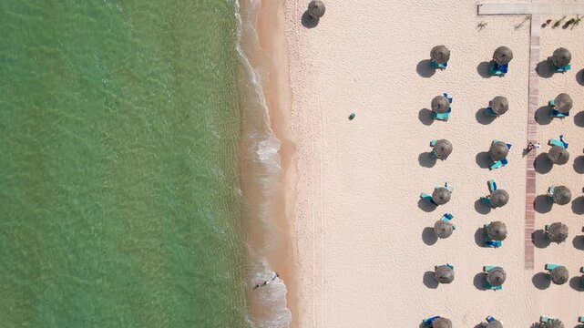 An aerial shot of a well-organized beach area with neatly arranged sun loungers and straw umbrellas. The sandy shore is clean and inviting, with gentle waves rolling onto the beach.