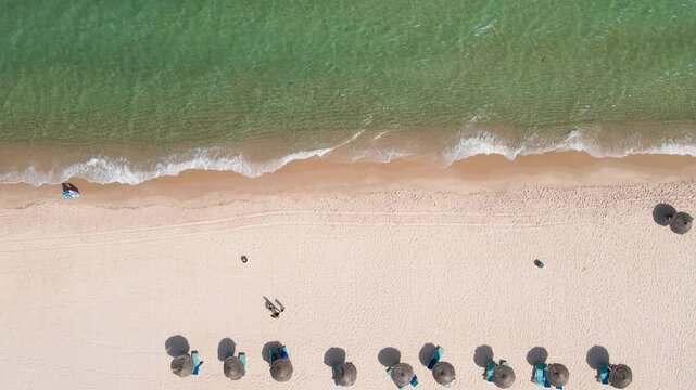 An overhead view of a calm beach with minimal activity, featuring a few scattered people enjoying the sand and sea. The clear water and soft waves create a peaceful setting ideal for solitude.