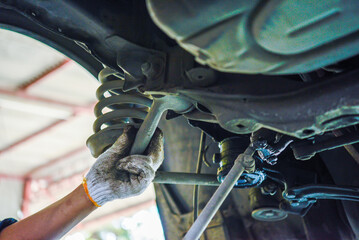 Close-up of a mechanic’s gloved hand using a wrench to adjust the suspension system underneath a...