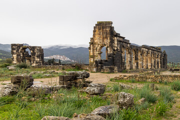 Caracallabogen und Basilika von Volubilis aus der r&ouml;mischen Antike und im Hintergrund Berge und die Stadt Moulay Idris in Marokko
