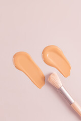Two cosmetic strokes of natural tone liquid foundation powder on a beige vertical background with a makeup brush. top view. copy space. texture sample