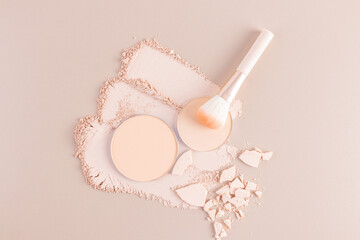 Three gorgeous strokes and a round block of compact powder in a natural tone on a beige background, a makeup brush, pieces of broken powder. top view