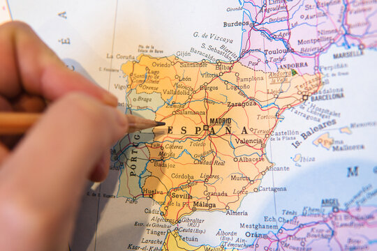 Close-up of a hand pointing at Spain on a map with a wooden pencil
