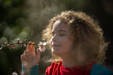 Child face close-up in spring park. Child enjoying spring sunshine. Child smelling flowers spring...