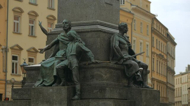 Close up of monument sculptures with historical yellow buildings in the background. Cracow Main Square, Poland. Adam Mickiewicz Statue Krakow.