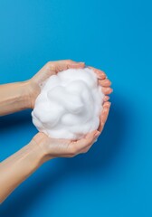 Hands holding a fluffy mound of white soap foam against a bright blue background