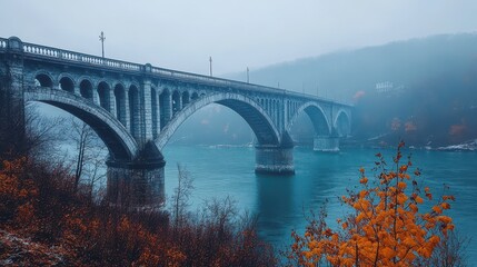 Obraz premium An architectural concrete arch bridge spans a wide misty turquoise river