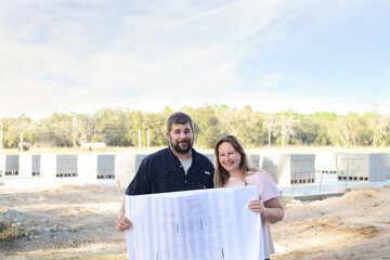 Smiling couple holding blueprints at their home construction sit