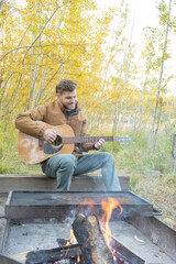 Fototapeta premium Man smiles and plays guitar while camping