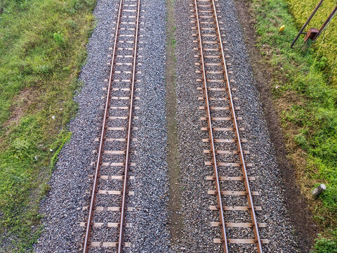 Symmetrical aerial view of dual railway tracks over gravel and surrounded by grassy terrain.