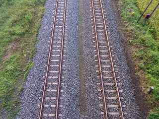 Symmetrical aerial view of dual railway tracks over gravel and surrounded by grassy terrain.