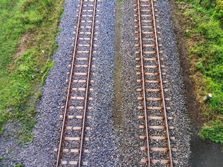 Symmetrical aerial view of dual railway tracks over gravel and surrounded by grassy terrain.