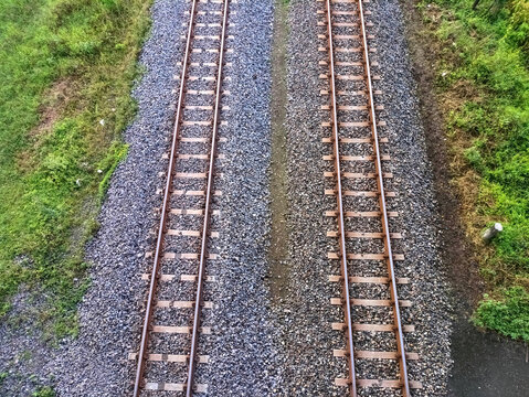 Symmetrical aerial view of dual railway tracks over gravel and surrounded by grassy terrain.